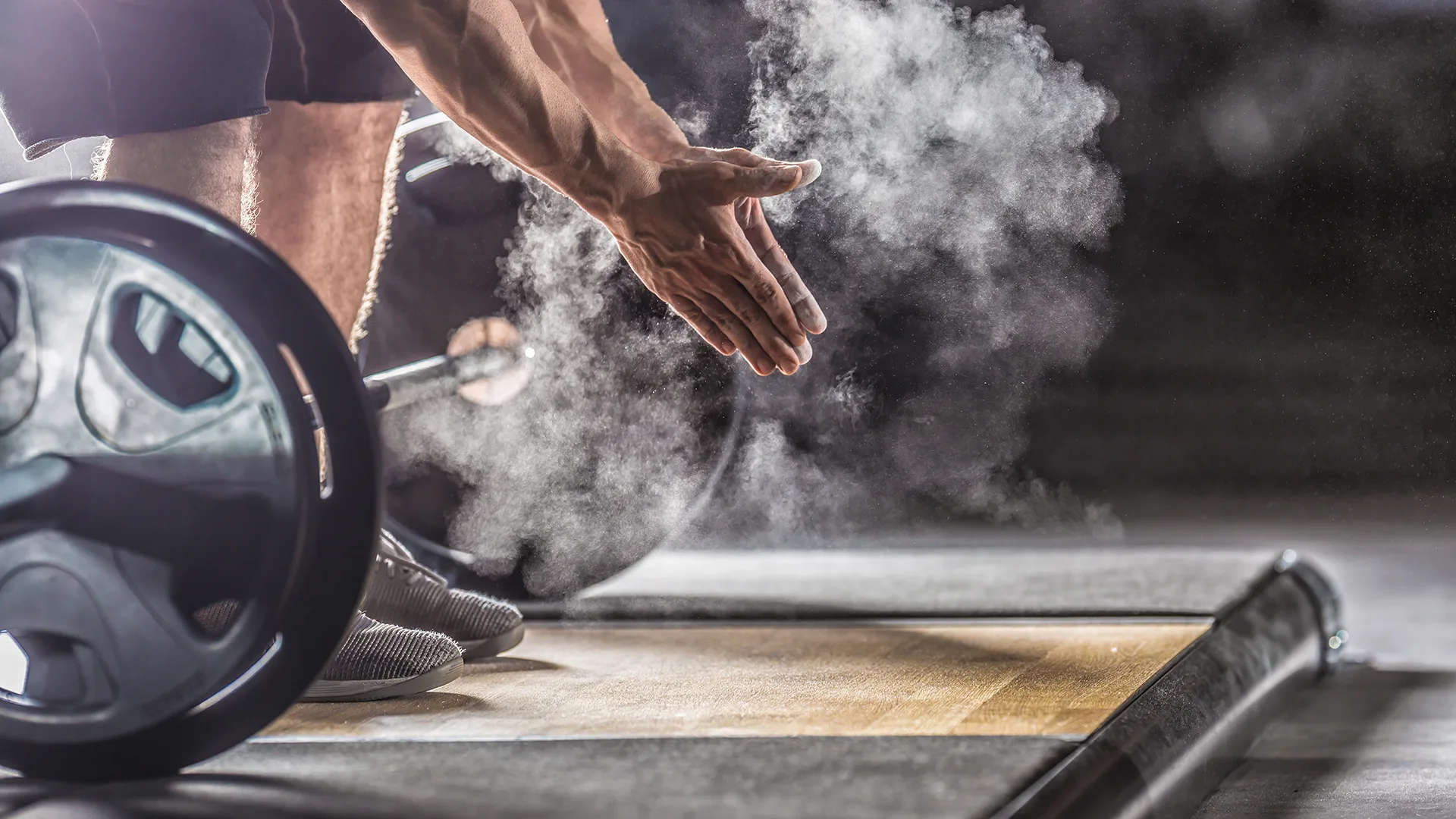 muscular weightlifter clapping hands before barbell workout at the gym with dumbbells